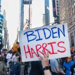 Person holding "Biden Harris" sign in crowded city street.