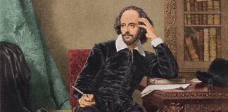 A seated man in period clothing, holding a quill, surrounded by books and a desk