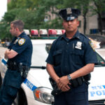 NYPD Sergeant CONVICTED — 11,000 Cops Fight Back… Two NYPD officers standing near a police car in an urban environment