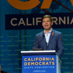 SWALWELL Facing Charges—Hired Illegal While Bashing Trump… Man speaking at California Democrats State Convention podium.