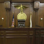 Kirk Murder CASE: Courtroom Openness UNDER ATTACK Judges bench in an empty courtroom, scales emblem above.