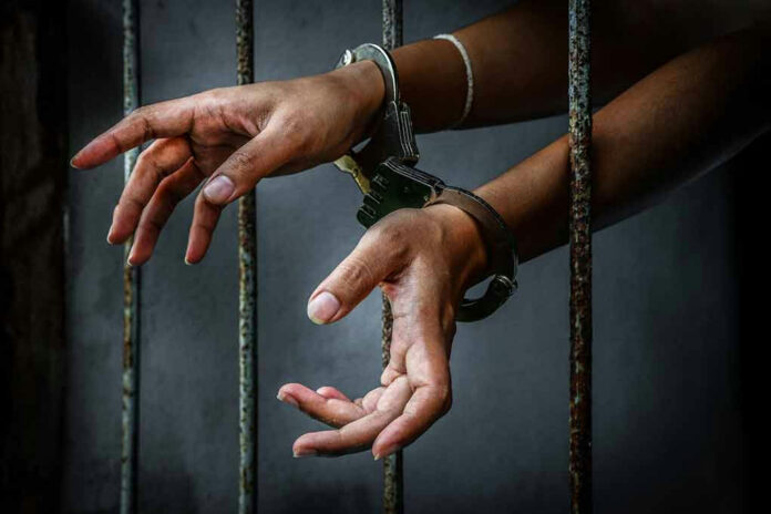 Handcuffed hands reaching through jail cell bars.