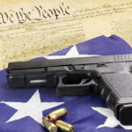 GUN BUYER SURVEILLANCE: New Law Shocks… Gun and bullets on American flag with Constitution background.