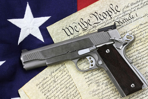 shutterstock129482747-1jpg Gun on U.S. Constitution with American flag background.