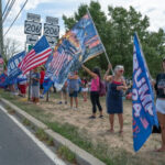 VIDEO: Vicious ATTACK at ‘Trump House’ Stuns Community… group of people holding flags at a roadside rally
