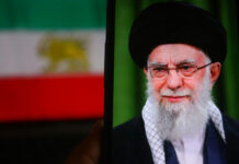 Iran’s War Chest FROZEN—What’s Missing? Person wearing glasses and turban in front of flag