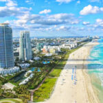 $50 Million Deal Sparks Foreign Influence STING… Aerial view of Miami Beach coastline and skyscrapers.