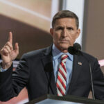 Man in suit speaks at podium with raised finger.