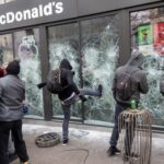 Protesters vandalizing a McDonald's restaurant with broken windows