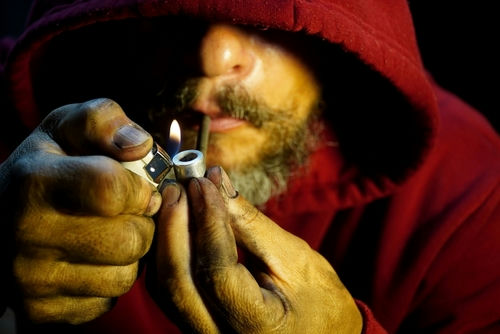 shutterstock_2213274683 Person igniting a pipe, wearing a red hoodie.