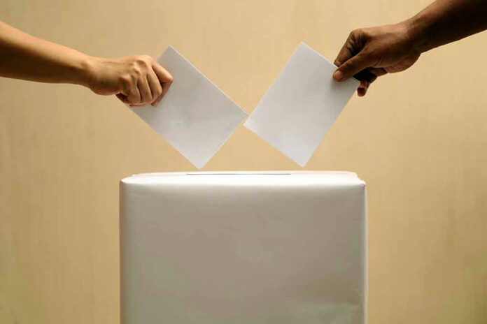 2395285153 Two hands placing ballots into a voting box.