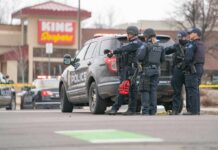 Police officers gather beside a patrol SUV at a taped-off scene
