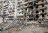 Damaged apartment building with debris scattered firefighters present.