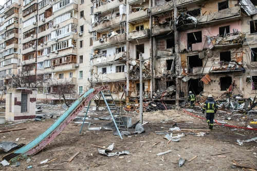 shutterstock_2129012939-2 Damaged apartment building with debris scattered firefighters present.