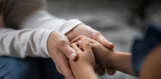 An adult hand holding a childs hand in a warm gesture