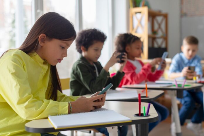 Diverse,Multiethnic,Kids,Students,Having,Break,And,Using,Smartphones,,Sitting Students using smartphones at classroom desks