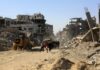 Told to Flee—Then the Bombs Fell People walk through a street of destroyed buildings and rubble