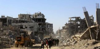 People walk through a street of destroyed buildings and rubble