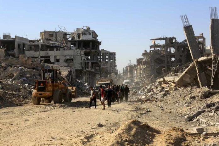 Palestinians,Return,To,Their,Homes,Following,A,Ceasefire,Agreement,Between People walk through a street of destroyed buildings and rubble