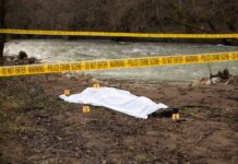 Crime scene near a river with covered body.