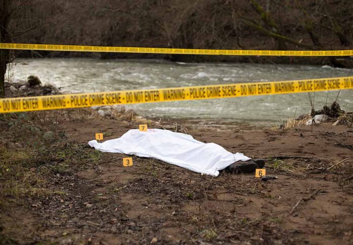 Crime scene near a river with covered body.