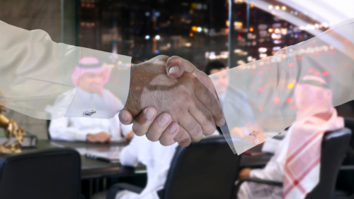 Two people shaking hands; men in background discussing.