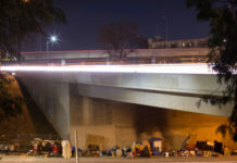 Homeless encampment under a highway overpass at night.