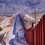 Border wall stretching through desert landscape with mountains.