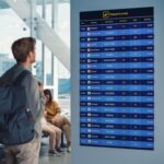 Person viewing flight departure board in busy airport terminal.