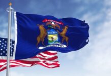 United States and Michigan flags waving against blue sky.