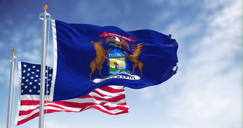 United States and Michigan flags waving against blue sky.