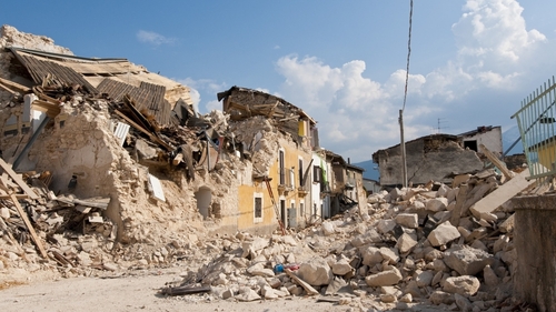 Rubble from collapsed buildings in earthquake-hit area. Clear sky.