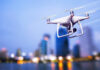 White drone flying over a cityscape at dusk.