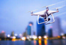 White drone flying over a cityscape at dusk.