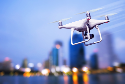 White drone flying over a cityscape at dusk.